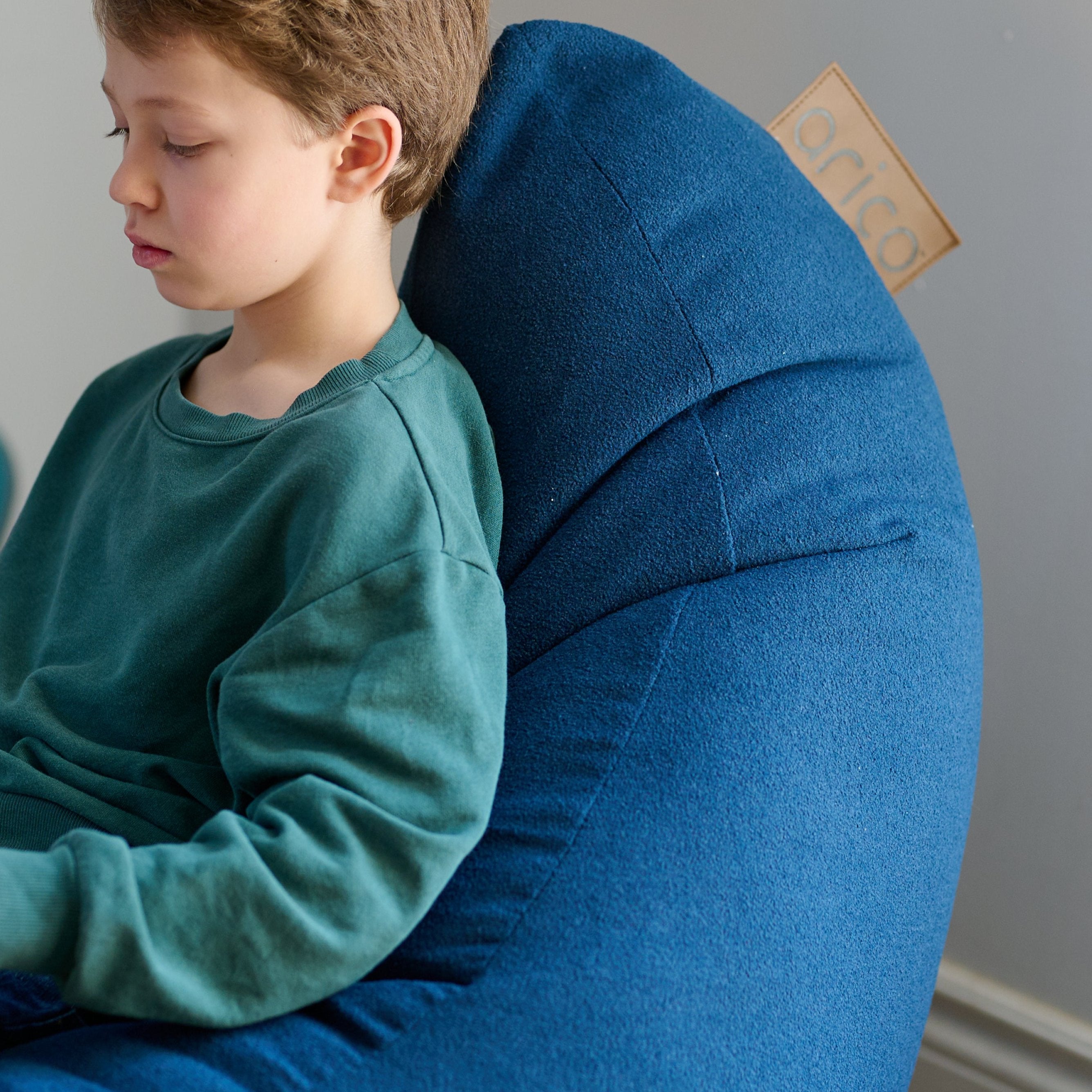 Gros plan sur un enfant lit un livre dans un bean bag ARICO, format Ergo Junior, assis confortablement, avec un support du bas du dos, jusqu'à la nuque, le bean bag le plus ergonomique sur le marché.