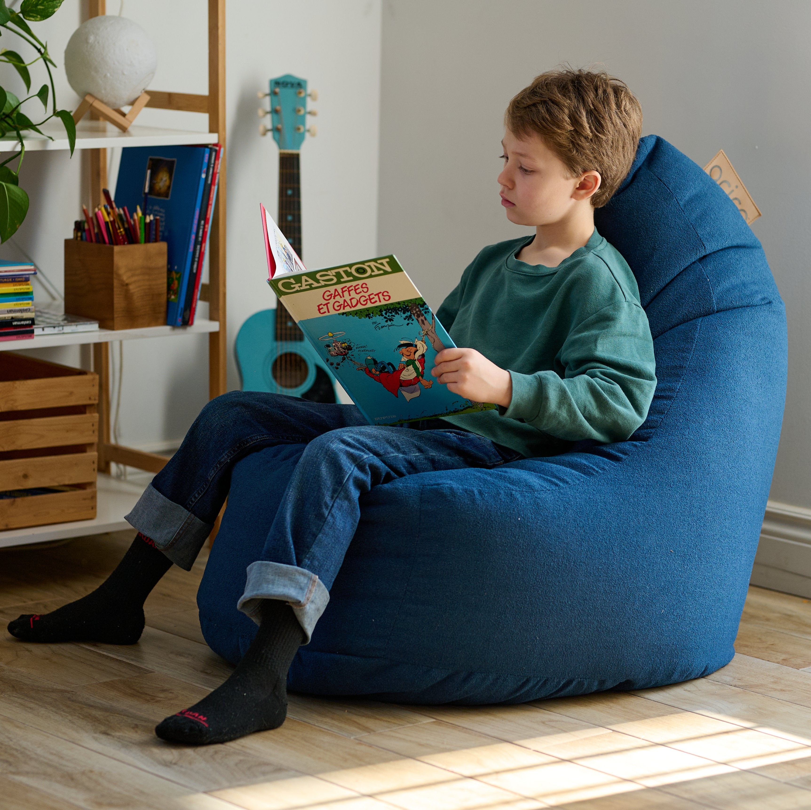 Un jeune enfant lit un livre dans un bean bag ARICO, format Ergo Junior, assis confortablement, avec un support du bas du dos, jusqu'à la nuque, le bean bag le plus ergonomique sur le marché.