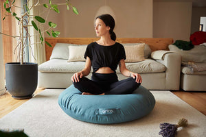 Coussin de sol TERRA de marque ARICO avec femme en position de méditation jambes croisés. 