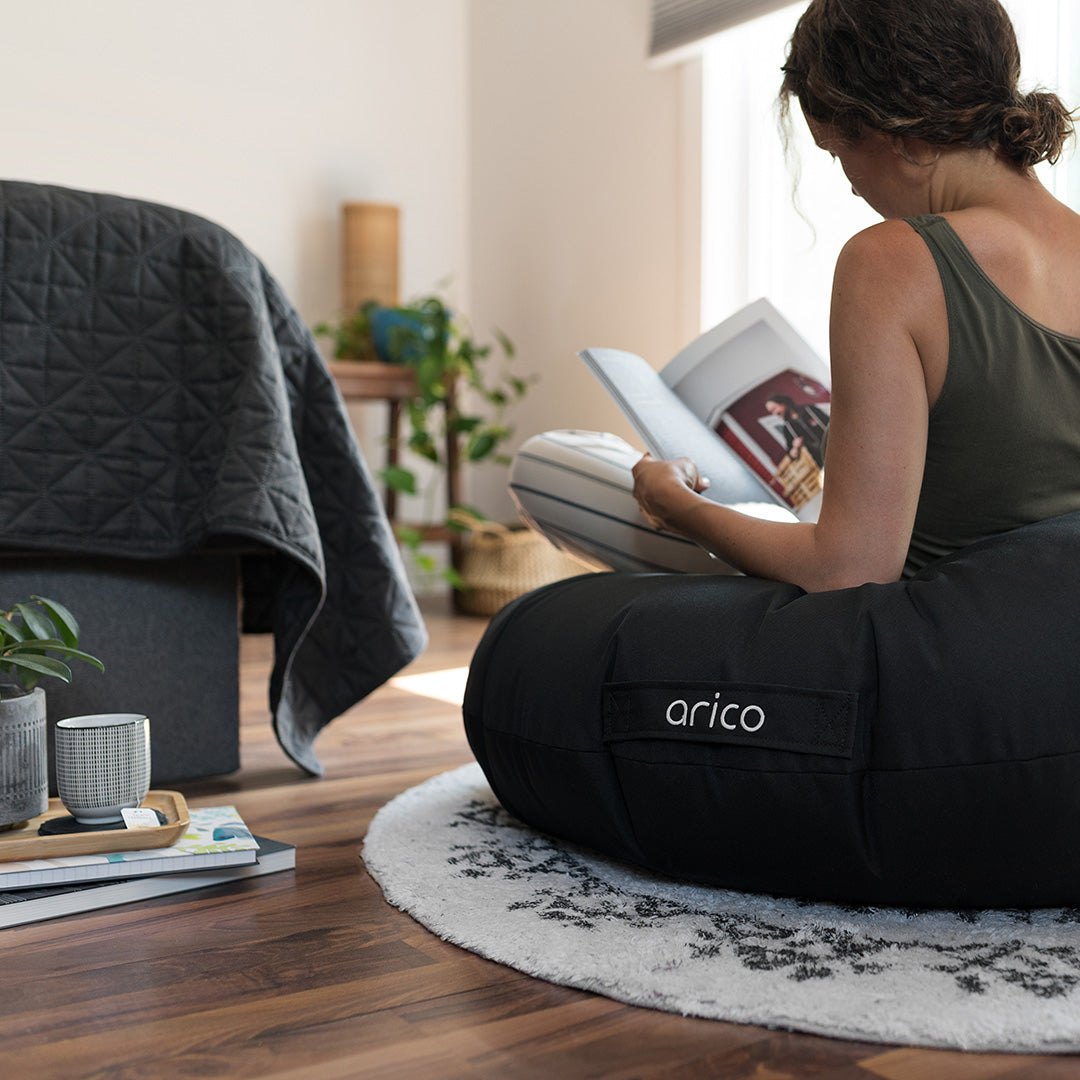 Coussin de sol Arico de couleur noir avec femme lisant dans un salon.