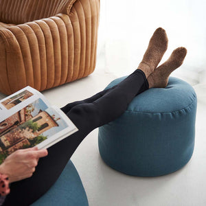 Image d'un pouf repose-pieds ARICO de couleur récif avec jambe de femme s'en servant comme repose-pieds. 