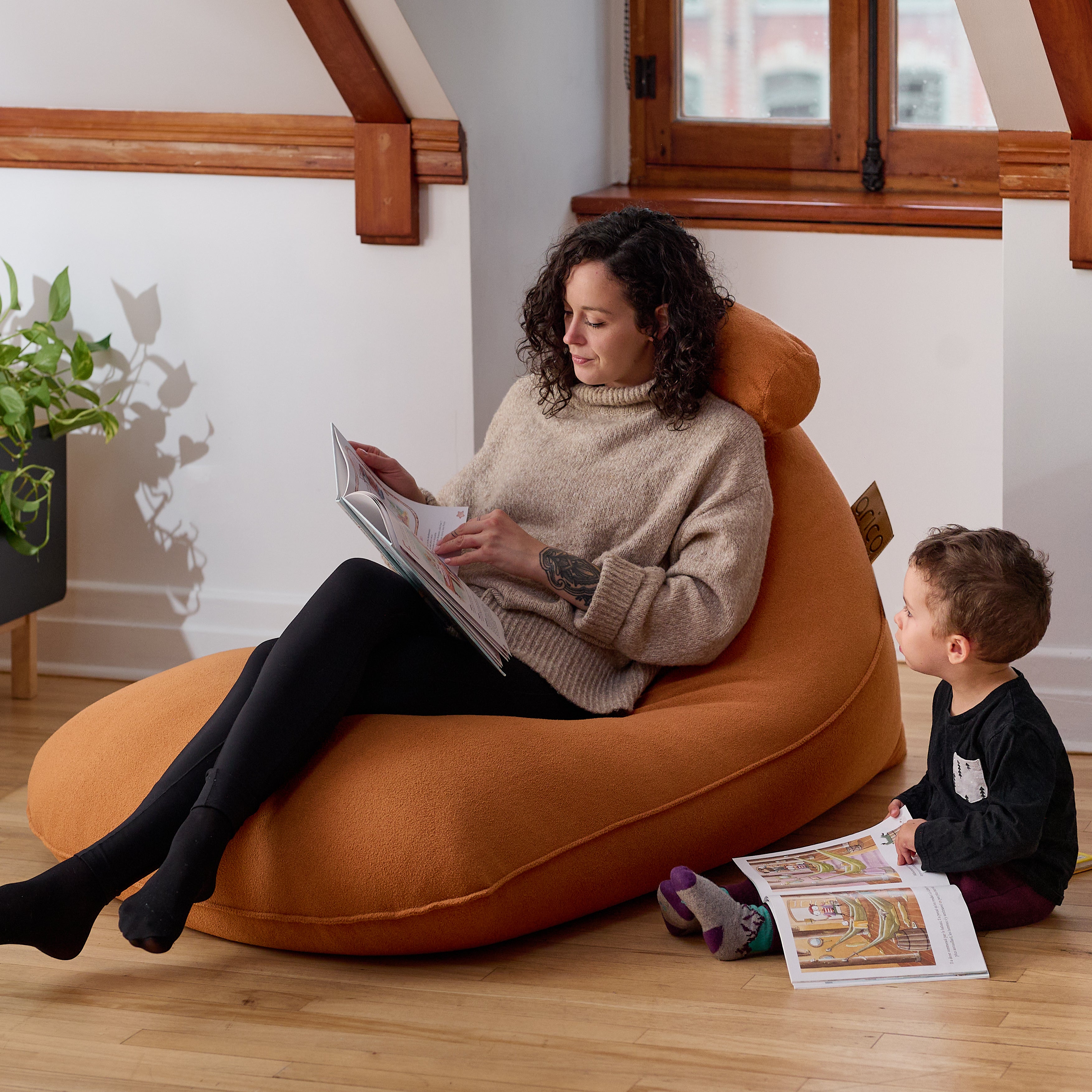 Une jeune femme lit un livre dans son bean bag de marque ARICO, coin détente.