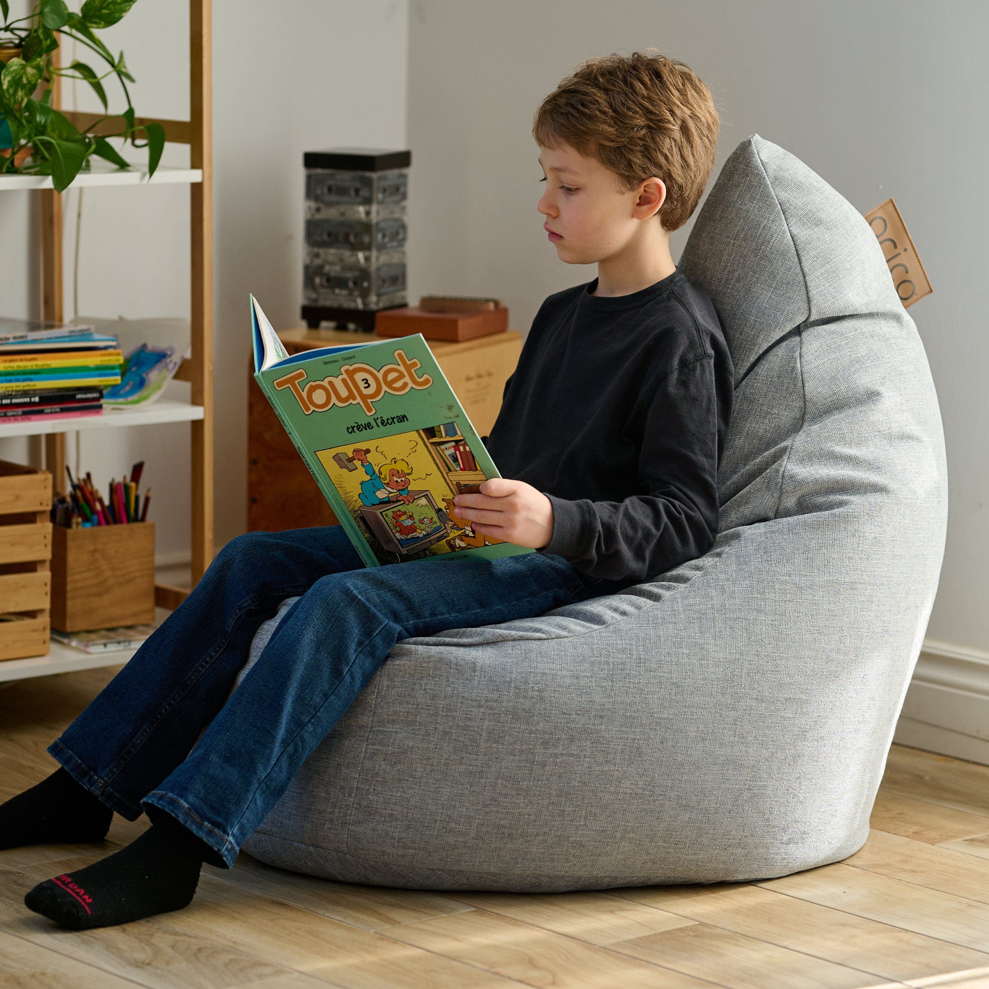 Photo d'ambiance avec un enfant qui lit un livre, assis avec une bonne posture dans son bean bag ARICO Ergo Junior.
