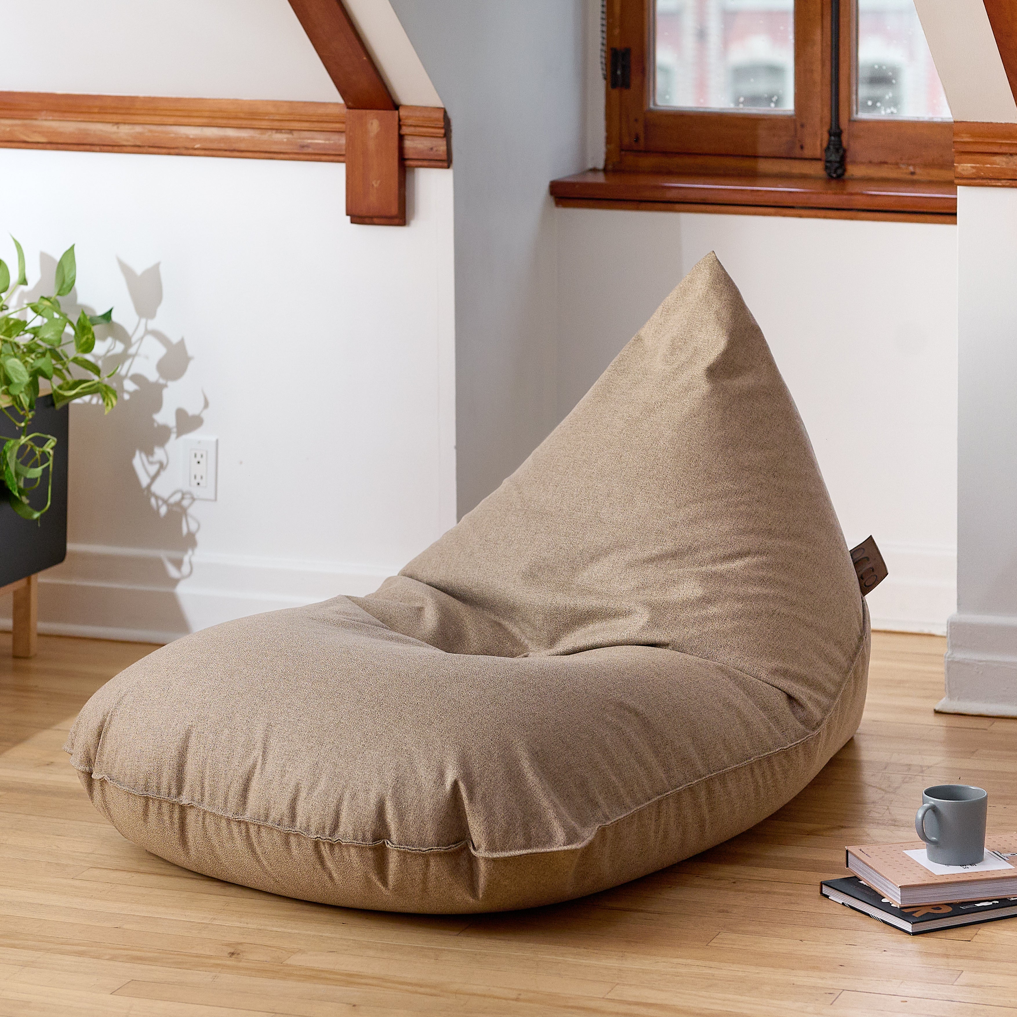 Bean bag Lounge Adulte ARICO beige parchemin dans un décor intérieur chaleureux avec plancher de bois, plante verte et coin détente. Fauteuil lounge confortable en tissu texturé, idéal pour lire, relaxer ou aménager un espace repos à la maison. Fabriqué au Canada.