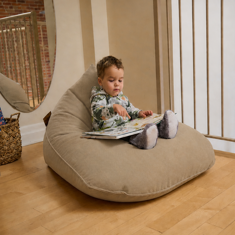 Enfant assis sur un bean bag Brun amande Paloma ARICO, lisant un livre dans un coin lecture chaleureux avec plancher de bois, miroir et rampe intérieure. Produit confortable pour enfant, fabriqué au Canada.