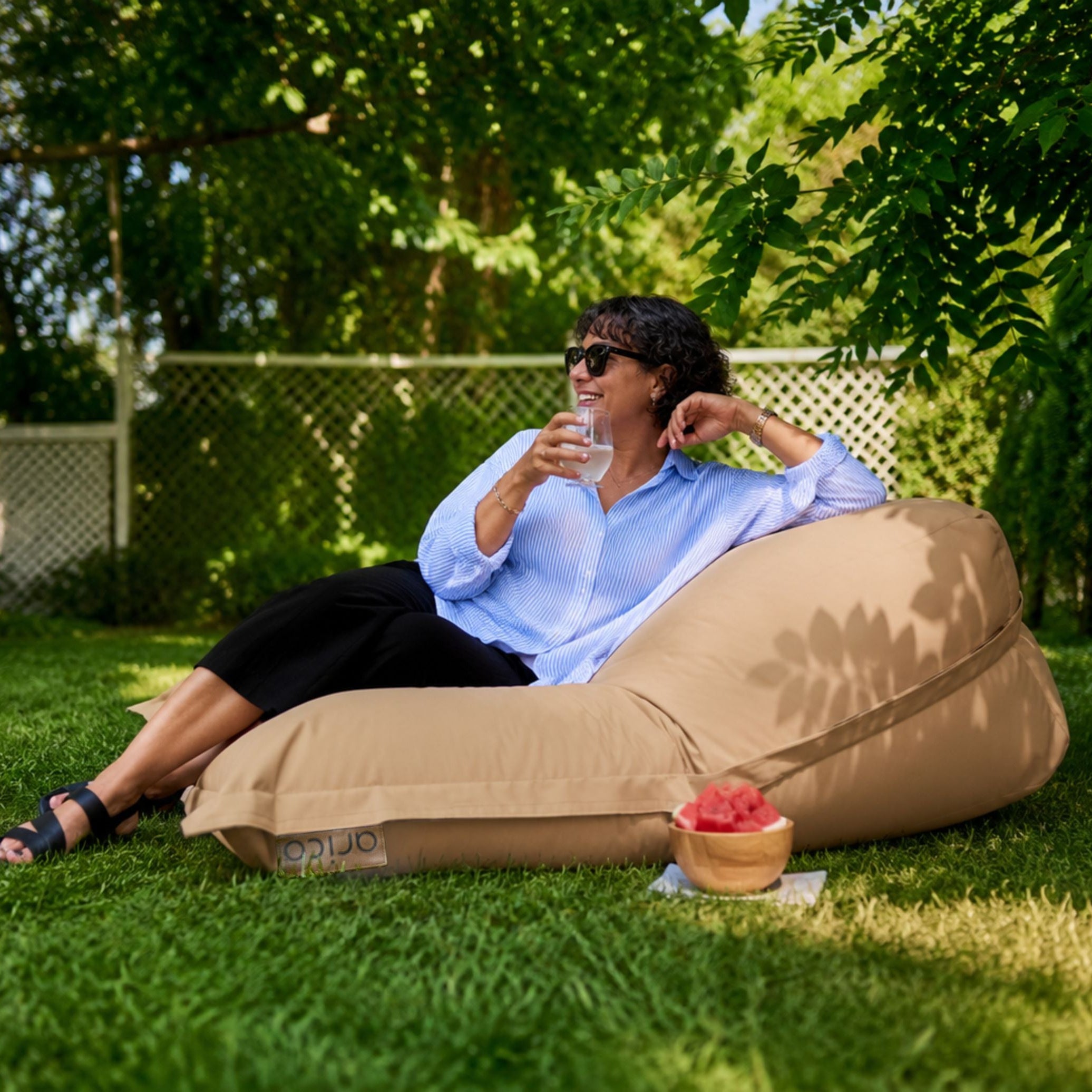 Femme dans un bean bag ARICO, au soleil, à l'extérieur, en train de boire un verre confortablement