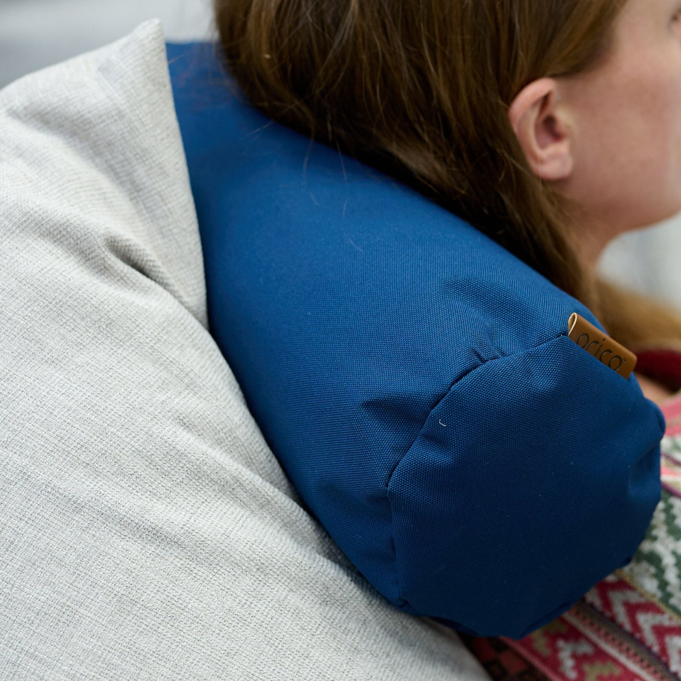 Jaune femme qui se détend avec un traversin ARICO derrière la nuque, pour une repos complet.