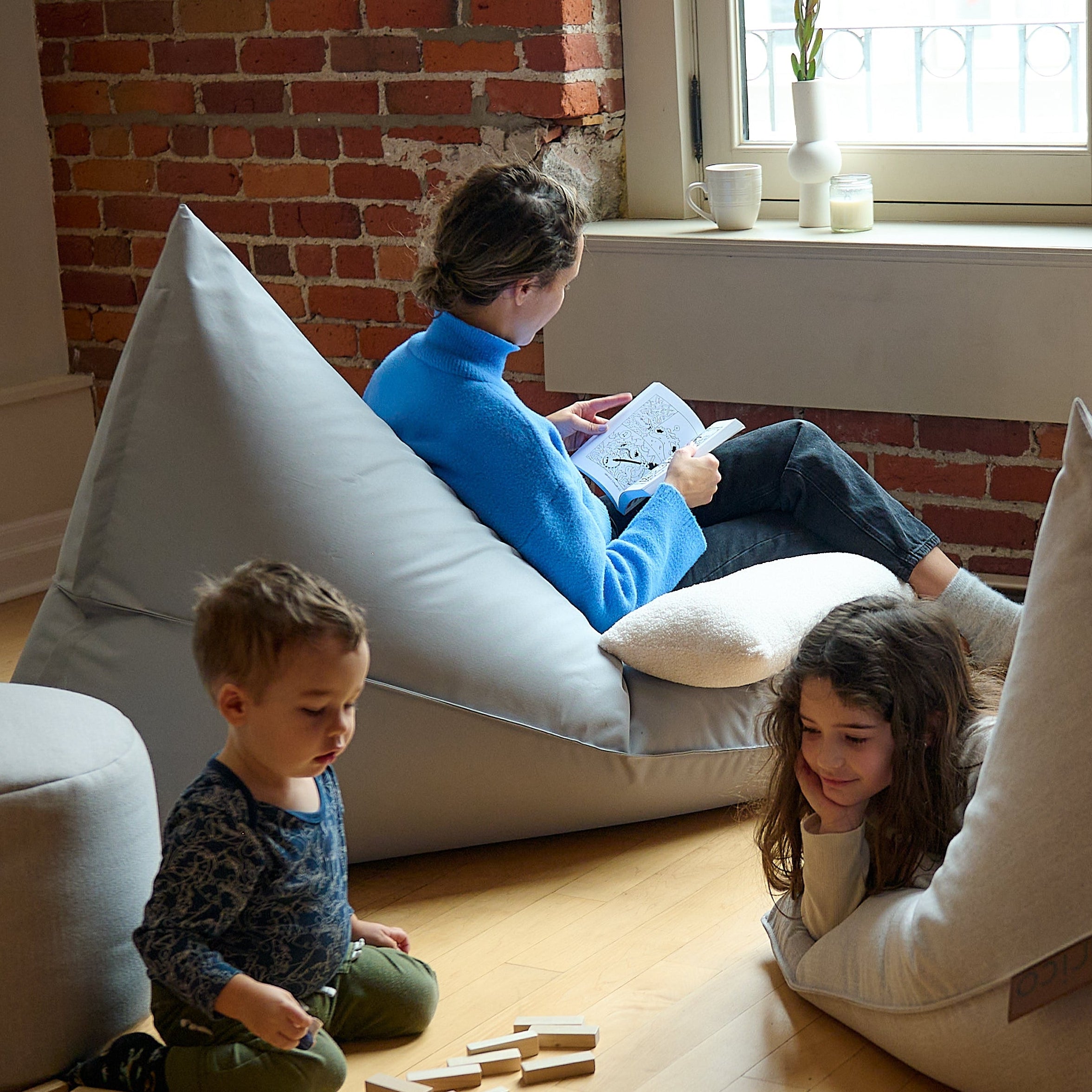 Environnement familial avec des enfants qui jouent au sol prêt d'une mère de famille qui lit un livre assise confortablement dans un bean bag Lounge Adulte ARICO