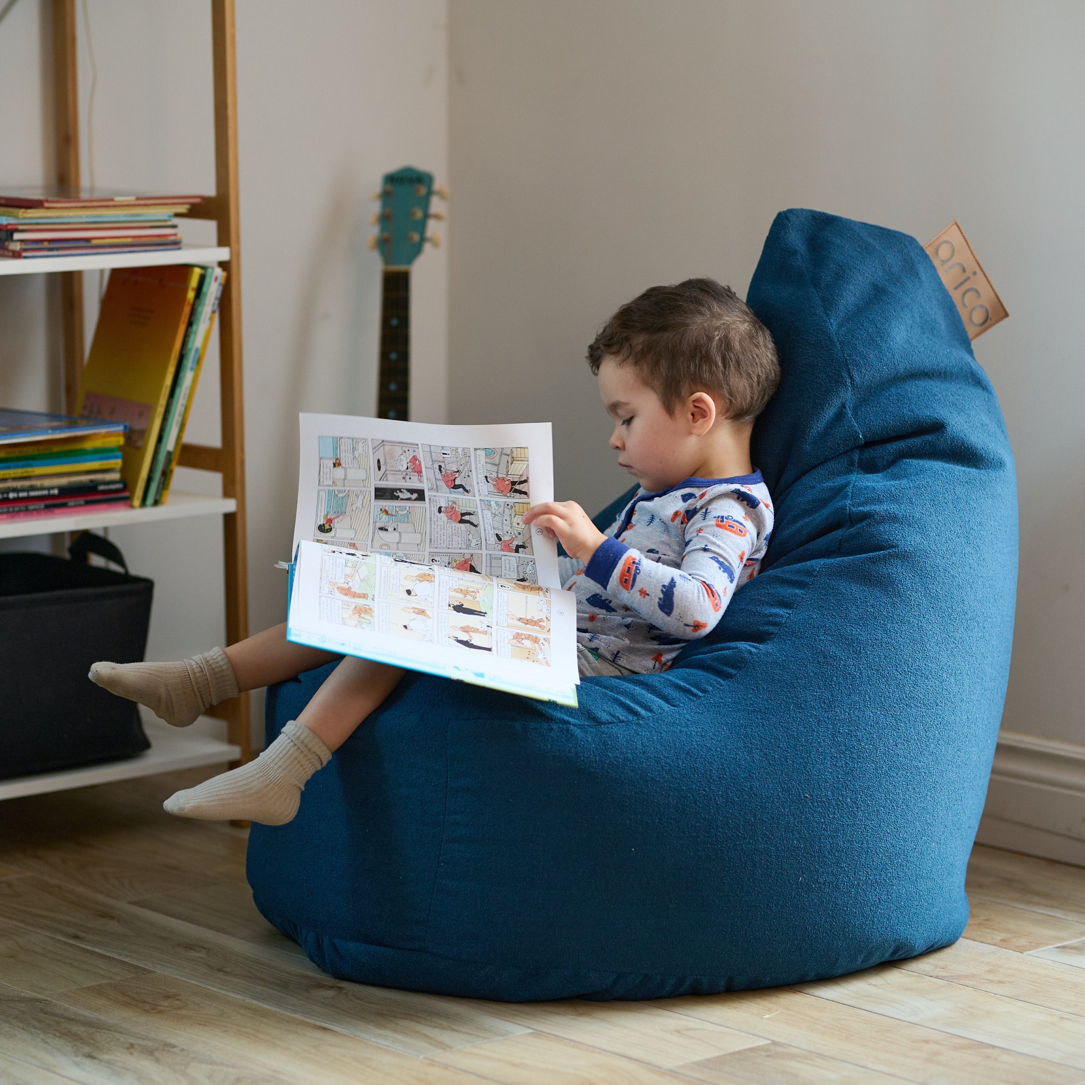Un jeune enfant lit un livre dans un bean bag ARICO, format Ergo Junior, assis confortablement, avec un support du bas du dos, jusqu'à la nuque, le bean bag le plus ergonomique sur le marché.