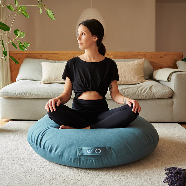 Coussin de sol Arico de couleur récif avec femme en position méditation. 